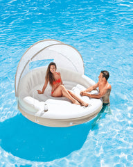 Two people on a circular inflatable pool float with canopy in a pool.